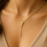 Vergoldete Y-Halskette mit funkelnden Zirkonia-Steinen am Hals einer Frau, eleganter Anhänger mit vier runden Fassungen, femininer Halsschmuck für Alltag und Anlass.
