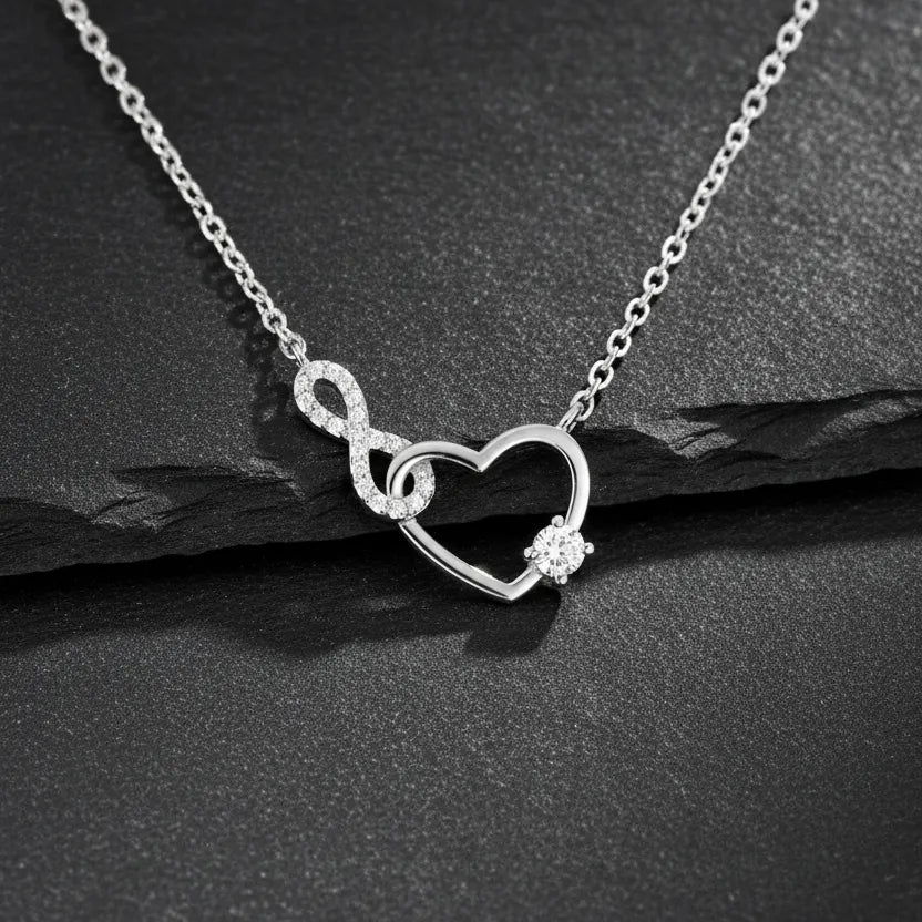 Feine Damen Halskette aus 925 Sterling Silber mit Herz-und-Unendlichkeitsanhänger, besetzt mit funkelnden Zirkonia und rundem Solitärstein, edel inszeniert auf schwarzem Schiefer.
