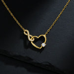 Vergoldete Damen Halskette mit offenem Herz- und Infinity-Anhänger, besetzt mit klar funkelnden Zirkonia und rundem Solitärstein, edel präsentiert auf dunklem Schieferhintergrund.
