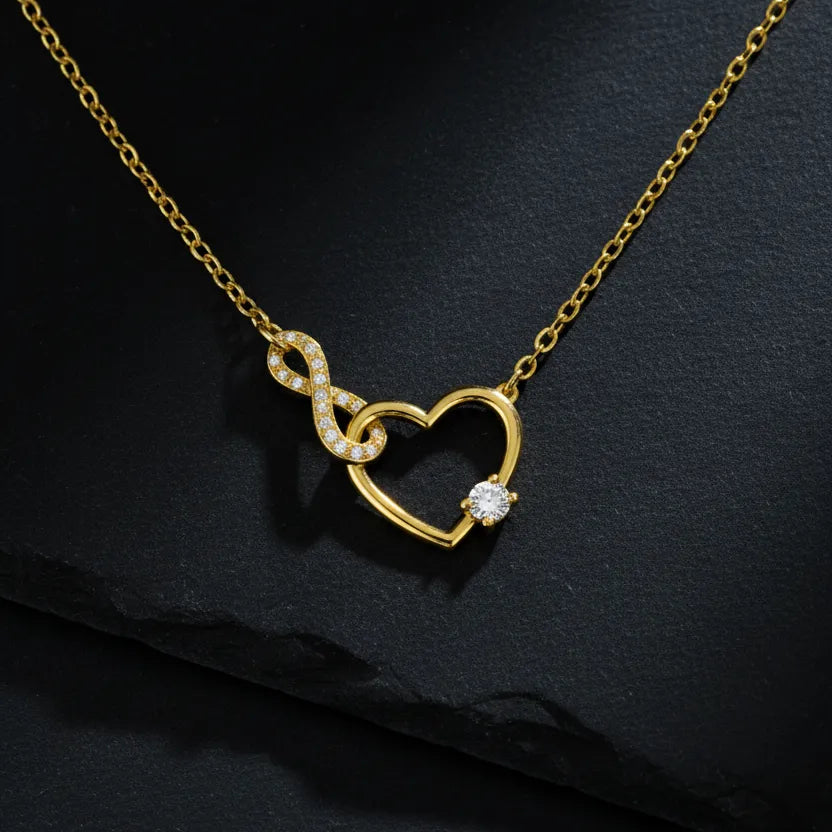 Vergoldete Damen Halskette mit offenem Herz- und Infinity-Anhänger, besetzt mit klar funkelnden Zirkonia und rundem Solitärstein, edel präsentiert auf dunklem Schieferhintergrund.
