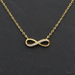 Vergoldete Damen Halskette mit filigranem Infinity-Anhänger, teilweise besetzt mit klar funkelnden Zirkonia-Steinen, elegant präsentiert auf dunklem Schieferhintergrund.
