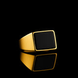 Goldener Herren-Siegelring mit schwarzem Achat, low-key Aufnahme auf schwarzem Hintergrund mit Spiegelung; edles IPG-Finish, dramatisches Licht, luxuriöser Premium-Look.
