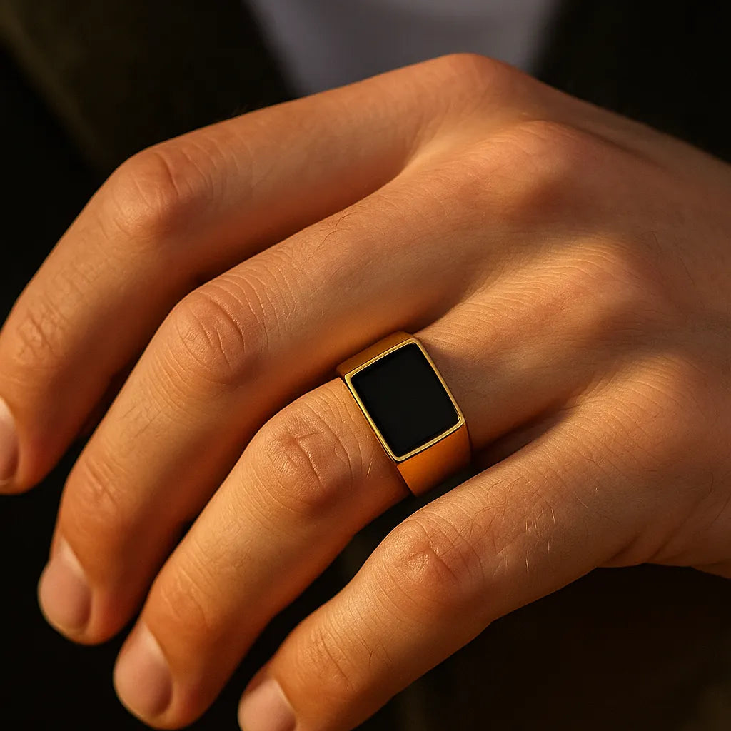 Herren-Siegelring aus vergoldetem Edelstahl mit rechteckigem schwarzem Stein, getragen am Ringfinger im Golden-Hour-Licht, Nahaufnahme.
