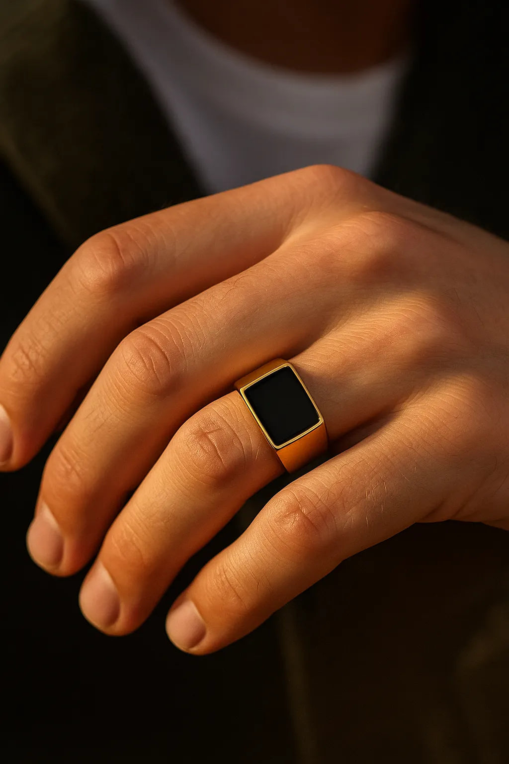 Herren-Siegelring aus vergoldetem Edelstahl mit rechteckigem schwarzem Stein, getragen am Ringfinger im Golden-Hour-Licht, Nahaufnahme.
