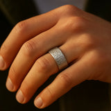 Herrenring aus Edelstahl, gehämmerte Oberfläche, breite Schiene – getragen am Ringfinger; Nahaufnahme im warmen Fensterlicht, natürliche Hauttöne.

