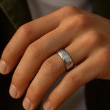 Herrenring Edelstahl silber, 7 mm breit, poliert – getragen am Ringfinger; Nahaufnahme im warmen Fensterlicht, natürliche Hauttöne, moderner Look.
