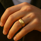 Herrenring vergoldeter Edelstahl, 8 mm, polierte Trauring-Optik – getragen am Ringfinger; Nahaufnahme im warmen Fensterlicht, natürliche Hauttöne.
