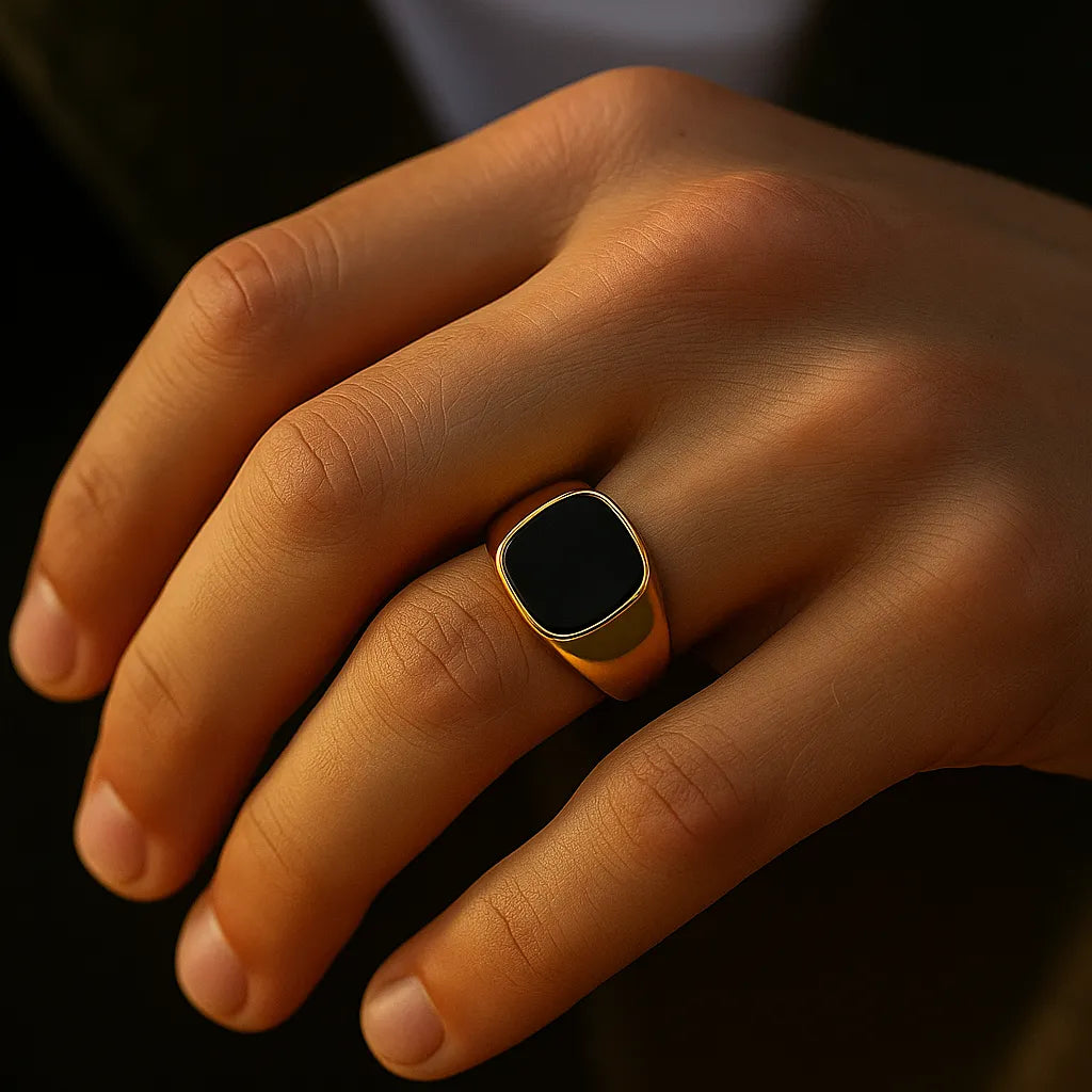 Herren-Siegelring aus vergoldetem Edelstahl mit schwarzem Achat, getragen am Ringfinger; Nahaufnahme im warmen Fensterlicht, natürliche Hauttöne, moderner Look.
