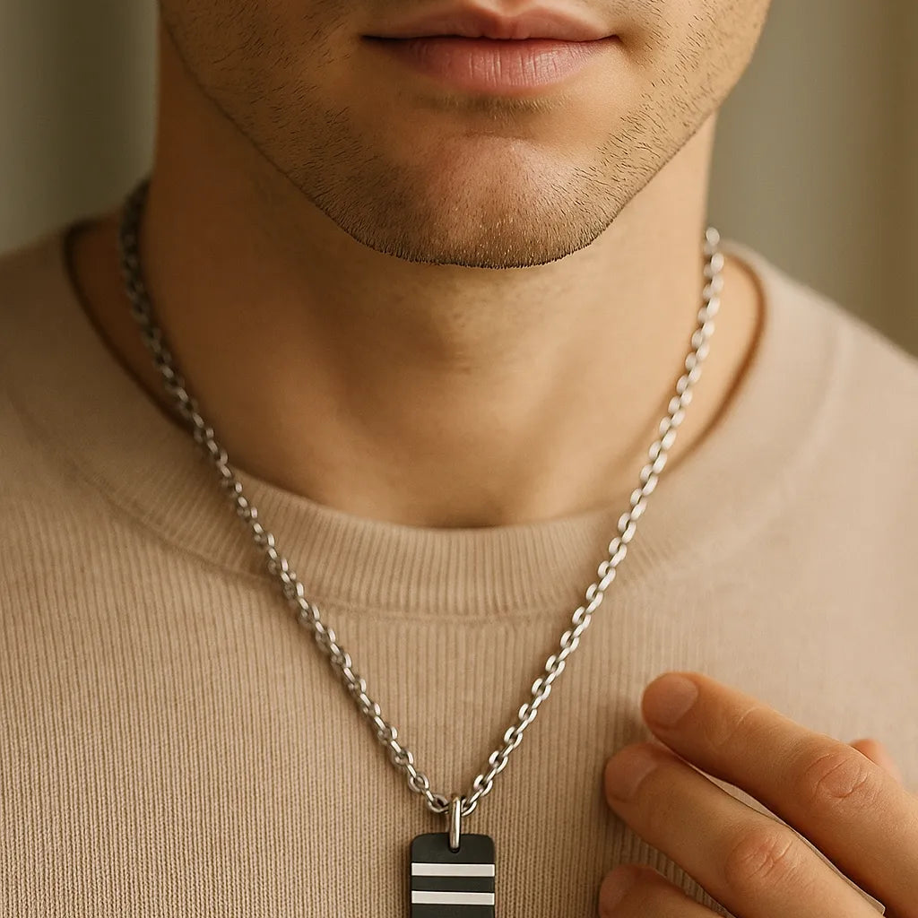 Nahaufnahme eines Mannes mit Herren-Halskette aus Edelstahl; schwarzer Carbon-Anhänger mit zwei silbernen Streifen, getragen über beigem Pullover, weiches Fensterlicht.

