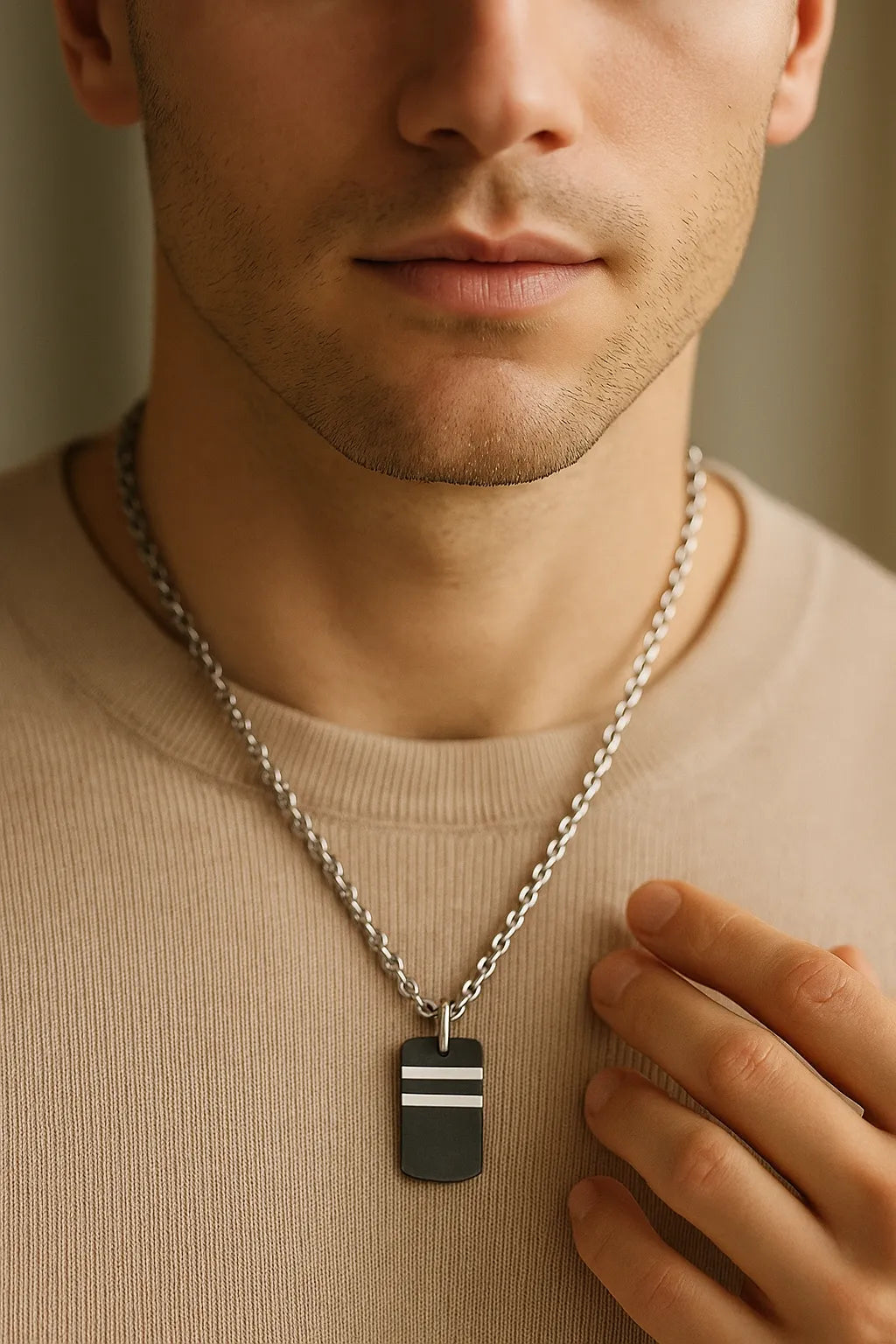 Nahaufnahme eines Mannes mit Herren-Halskette aus Edelstahl; schwarzer Carbon-Anhänger mit zwei silbernen Streifen, getragen über beigem Pullover, weiches Fensterlicht.
