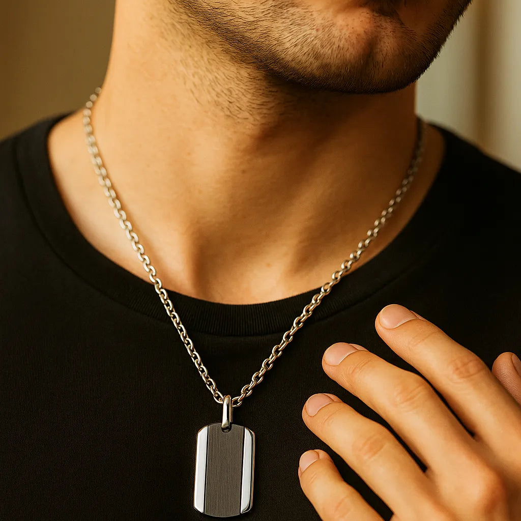 Herren-Halskette aus Edelstahl mit Dogtag-Anhänger in schwarzem Carbon-Look, getragen am Hals; Nahaufnahme im warmen Fensterlicht, moderner Minimal-Stil.
