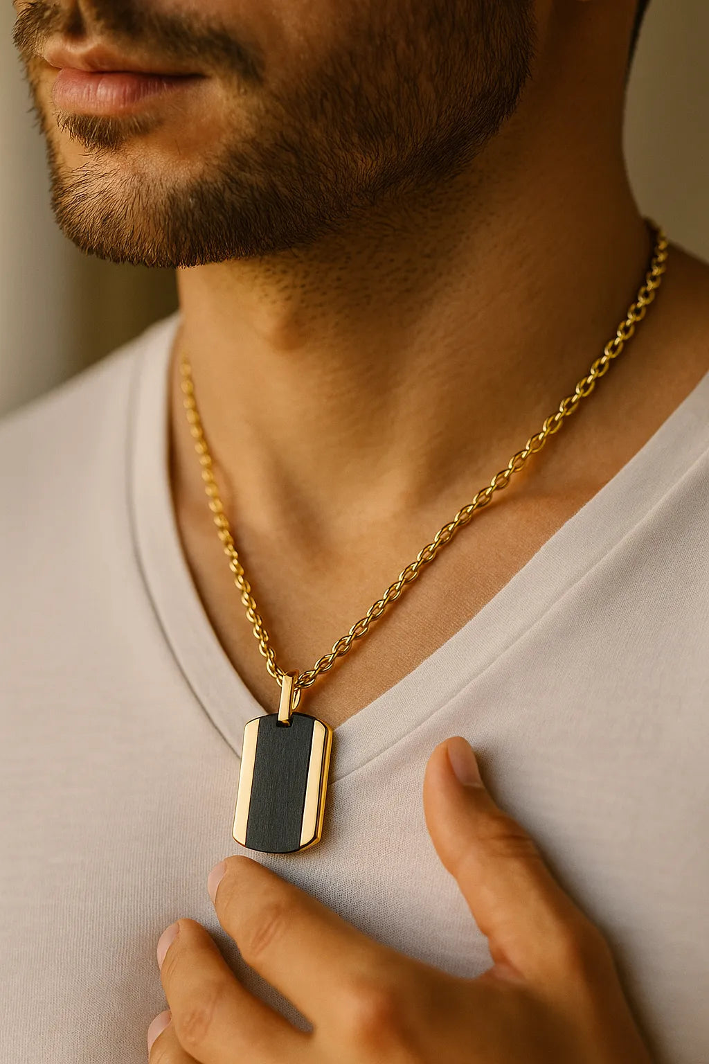 Herren-Halskette: vergoldete Edelstahlkette mit zweifarbigem Dogtag (schwarz/gold), getragen am Hals eines Mannes im warmen Fensterlicht, nah aufgenommen.
