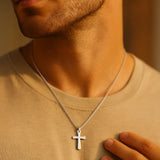 Silberne Herren-Kreuzkette aus Edelstahl, authentisch am Hals getragen bei Golden-Hour-Licht, weiche Unschärfe für edlen Fashion-Look.