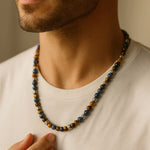 Herren Halskette mit Sodalith- und Tigerauge-Perlen, Edelstahl-Spacer; getragen am Hals eines Mannes im warmen Fensterlicht, Nahaufnahme mit neutralem Hintergrund.
