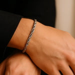 Herren-Armband aus Edelstahl, Rope-Chain/Seilkette, getragen am Handgelenk; Nahaufnahme im sanften Fensterlicht, dezente Maniküre, moderner Minimal-Look.
