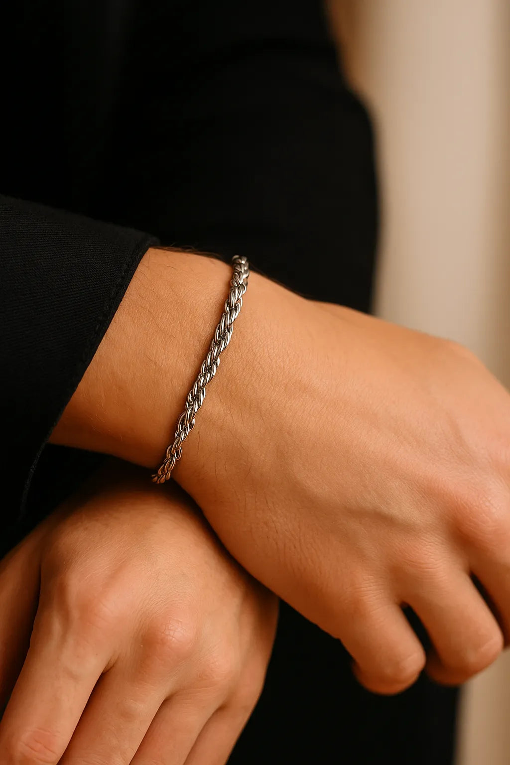 Herren-Armband aus Edelstahl, Rope-Chain/Seilkette, getragen am Handgelenk; Nahaufnahme im sanften Fensterlicht, dezente Maniküre, moderner Minimal-Look.
