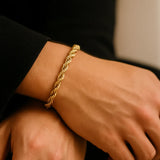 Herren-Armband vergoldeter Edelstahl, Rope-Chain/Seilkette am Handgelenk; Nahaufnahme im sanften Fensterlicht, polierte Twisted-Glieder, moderner Premium-Look.
