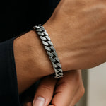 Herren-Armband aus Edelstahl, massive Panzerkette am Handgelenk eines Mannes; Nahaufnahme im natürlichen Fensterlicht, gebürstet/poliert, moderner maskuliner Stil.
