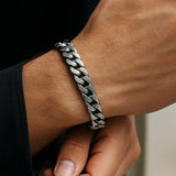 Herren-Armband aus Edelstahl, massive Panzerkette am Handgelenk eines Mannes; Nahaufnahme im natürlichen Fensterlicht, gebürstet/poliert, moderner maskuliner Stil.
