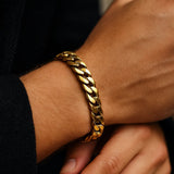 Herren-Armband, vergoldete Edelstahl-Panzerkette am Handgelenk; Nahaufnahme im warmen Fensterlicht, polierte Glieder, dezente Maniküre, moderner Premium-Look.