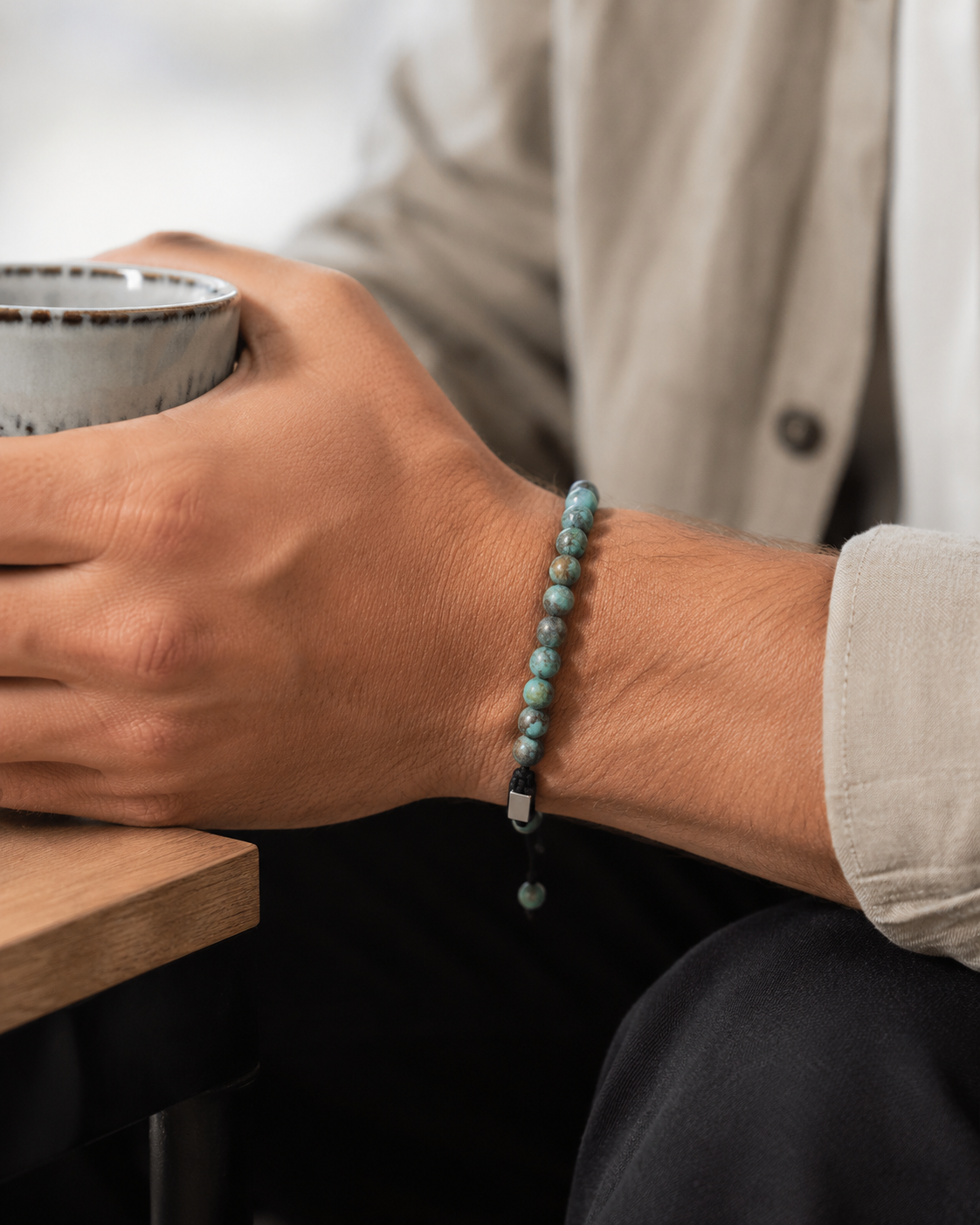 SON Herrenarmband aus 6 mm African-Turquoise-Perlen, alltagstauglich getragen mit beigem Hemd und Keramiktasse