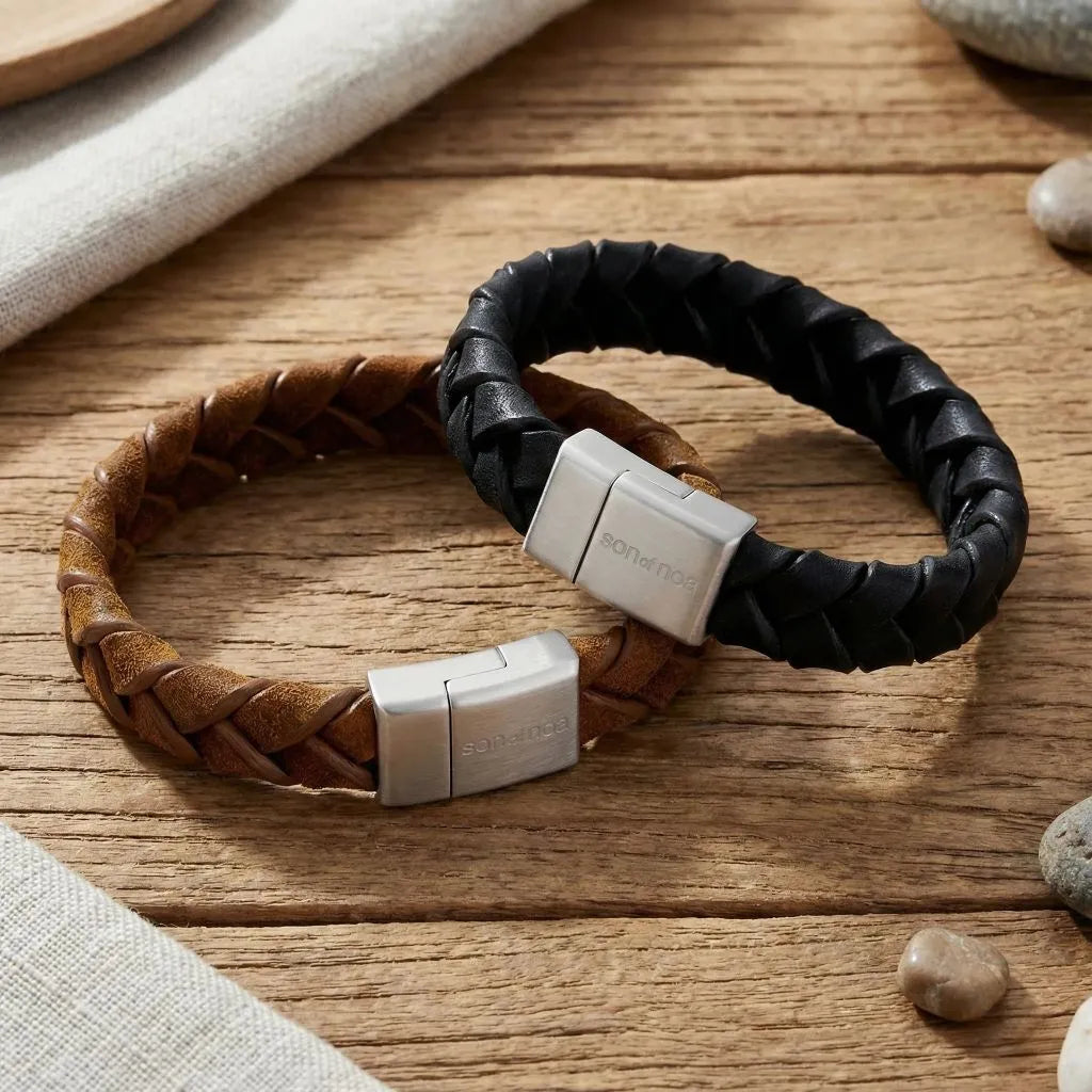 „Zwei geflochtene Herren-Lederarmbänder in Braun und Schwarz mit Edelstahl-Magnetverschluss von Son of Noa auf rustikalem Holzhintergrund.“
