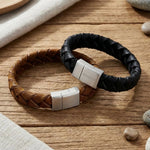 „Zwei geflochtene Herren-Lederarmbänder in Braun und Schwarz mit Edelstahl-Magnetverschluss von Son of Noa auf rustikalem Holzhintergrund.“
