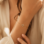 Feminines PamelaNor Armband mit zartem Goldglanz und funkelndem Kleeblatt-Motiv in warmer natürlicher Lichtstimmung.