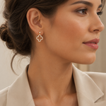 PamelaNor Ohrhänger aus vergoldetem 925 Silber mit funkelndem Kleeblatt-Design, elegant zu hellem Blazer getragen.