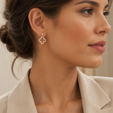 PamelaNor Ohrhänger aus vergoldetem 925 Silber mit funkelndem Kleeblatt-Design, elegant zu hellem Blazer getragen.