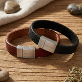„Zwei glatte Herren-Lederarmbänder in Braun und Schwarz mit breitem Edelstahl-Magnetverschluss von Son of Noa auf rustikalem Holztisch.“