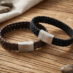 „Zwei Herren-Lederarmbänder von Son of Noa im schwarzen und braunen Fischgrätenmuster mit Edelstahl-Magnetverschluss auf rustikalem Holztisch.“
