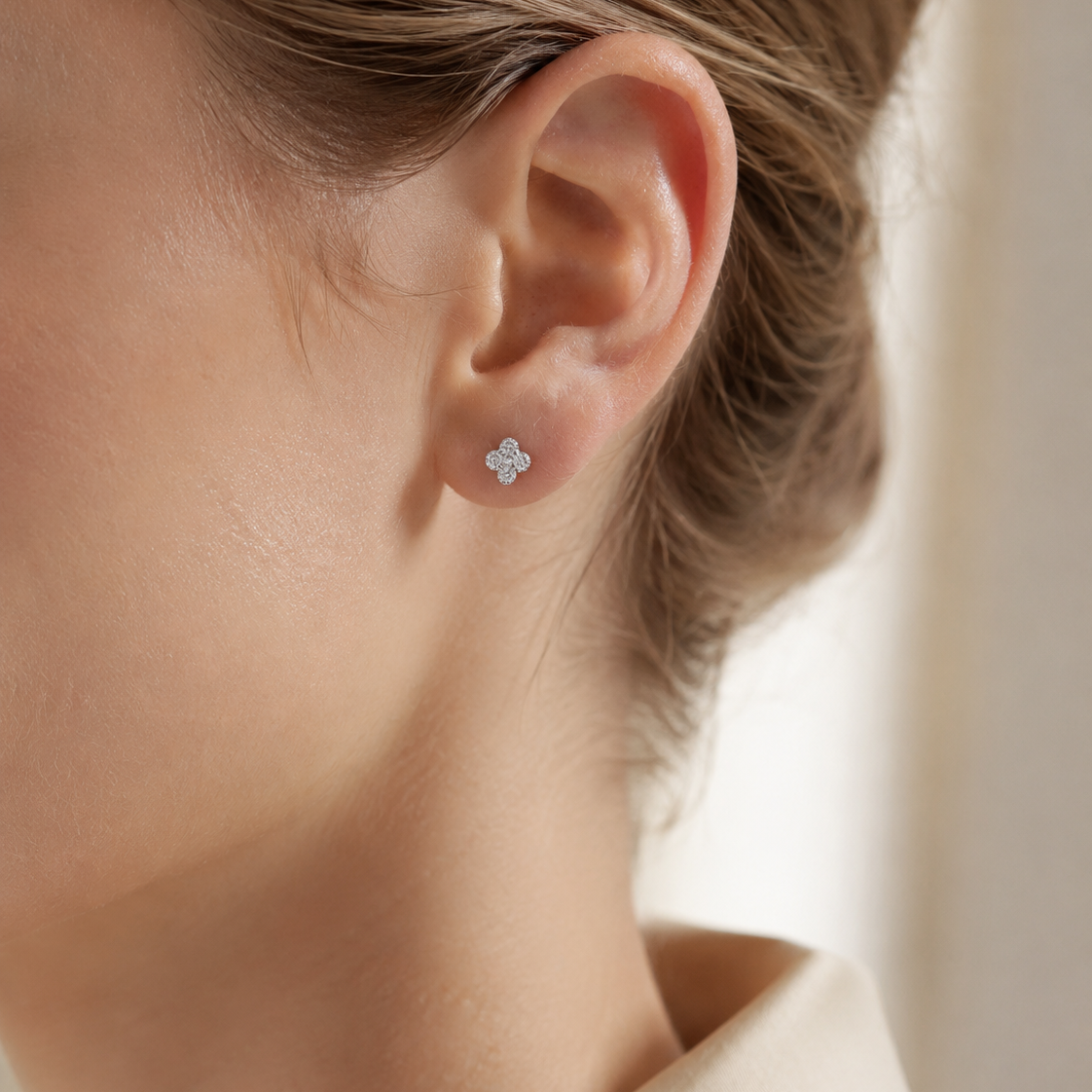 SigneNor Ohrstecker aus 925 Sterling Silber in zarter Kleeblattform an elegantem Ohr, getragen im cleanen Beauty-Look mit cremefarbener Bluse.