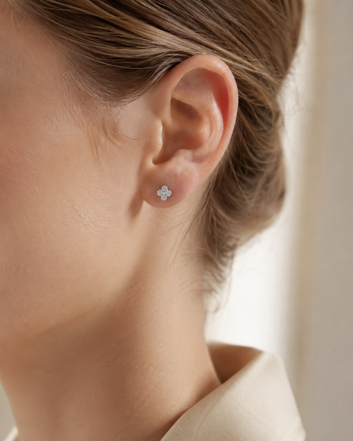 SigneNor Ohrstecker aus 925 Sterling Silber in zarter Kleeblattform an elegantem Ohr, getragen im cleanen Beauty-Look mit cremefarbener Bluse.