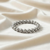 Ein Armband aus grauen Perlen auf einem glatten, hellen Stoff.