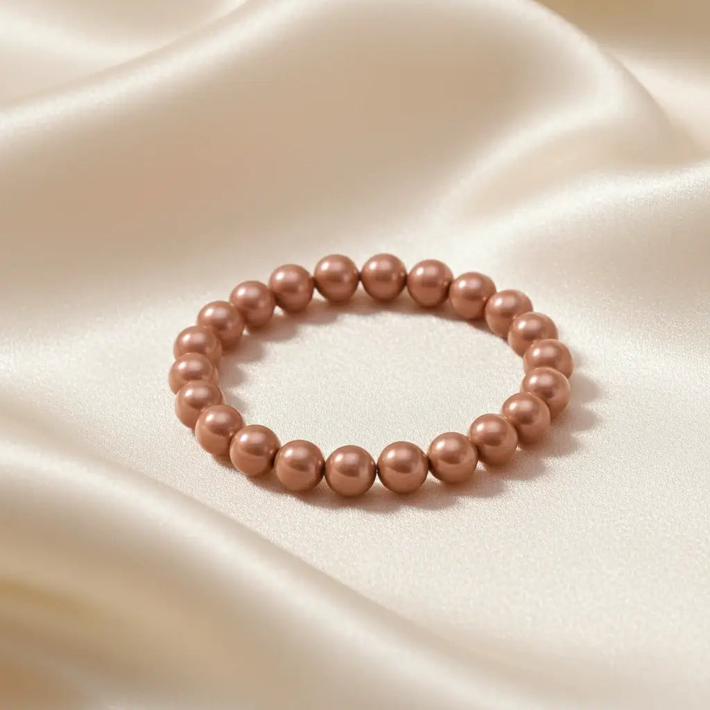 Ein Armbands aus glänzenden, terrakottafarbenen Perlen, das auf einem beigefarbenen, seidenartigen Stoff liegt.