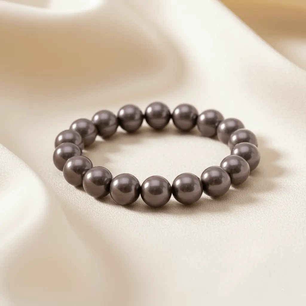 Ein Armband aus dunkelgrauen Perlen auf einem glatten, hellen Stoff.