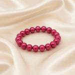 Ein fuchsiafarbenes Perlenarmband liegt auf einem beigefarbenen, seidigen Stoff.