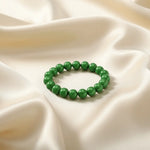 Ein Armband aus grünen Perlen auf einem glatten, hellen Stoff.