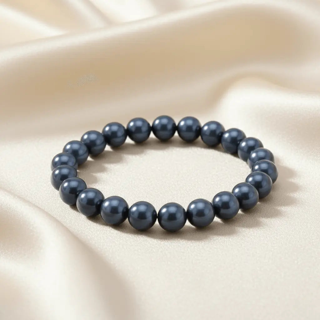 Ein Armband aus blaugrauen Perlen auf einem glatten, hellen Stoff.