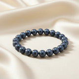 Ein Armband aus blaugrauen Perlen auf einem glatten, hellen Stoff.