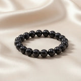 Ein Armband aus dunkel grauen Perlen auf einem glatten, hellen Stoff.