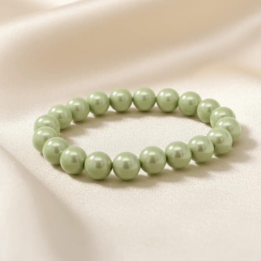 Ein Armbands aus hellgrünen, glänzenden Perlen, das auf einem beigefarbenen, seidenartigen Stoff liegt.