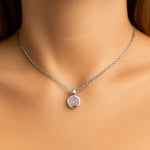 Nahaufnahme eines Frauenhalses mit einer silbernen Kette und einem kleinen, runden Rosenquarz-Anhänger von 5 mm Durchmesser. Der zartrosa, leicht trübe facettierte Stein ist in einer glänzenden Silberfassung eingefasst. Der Hintergrund ist neutral und weich ausgeleuchtet, der Fokus liegt auf dem Anhänge