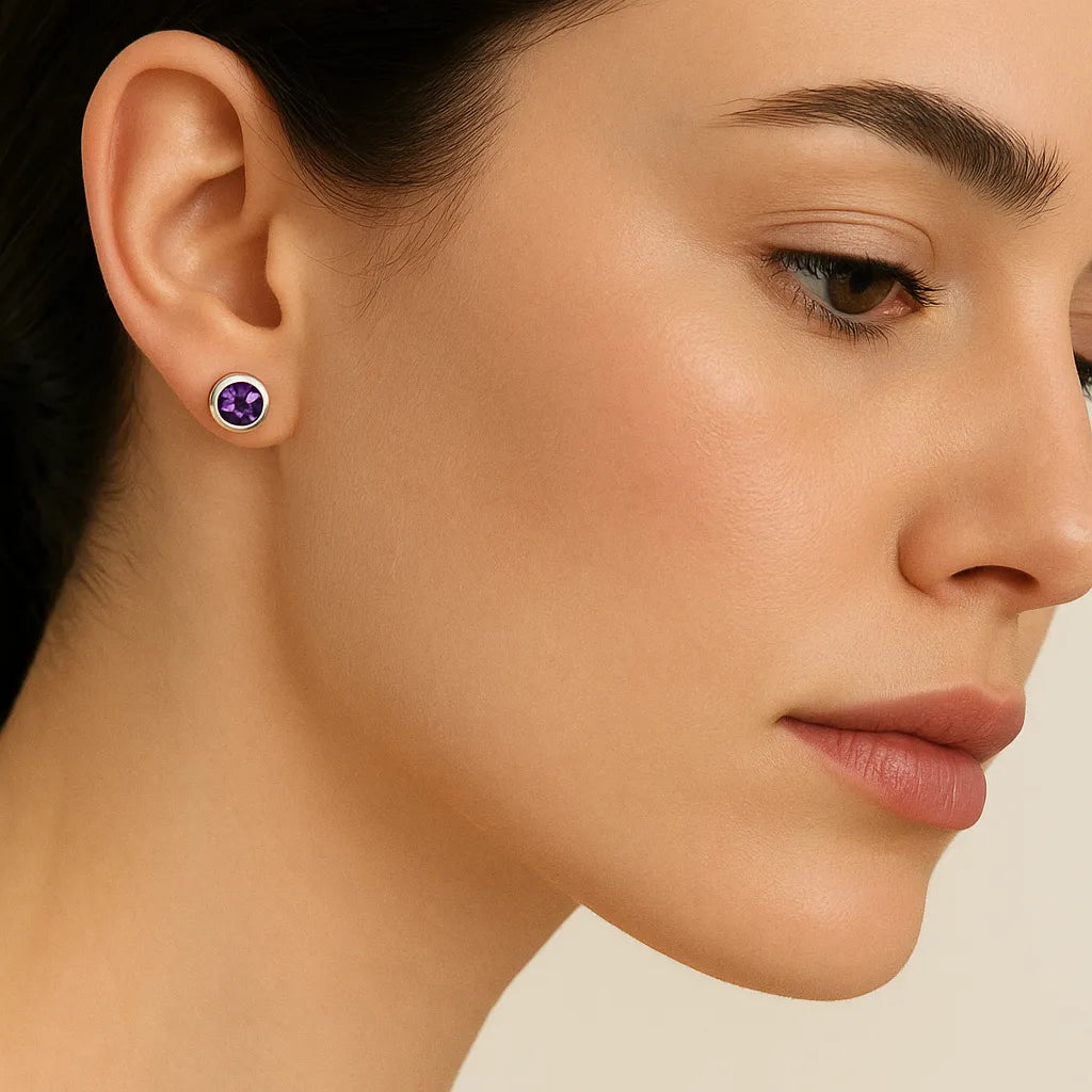 Porträt einer Frau in Seitenansicht, die einen silbernen Ohrstecker mit einem runden, facettierten Amethyst trägt. Der violette Edelstein funkelt dezent im Licht, während die Frau mit glatter Haut und dezentem Make-up vor einem neutralen Hintergrund zu sehen ist.