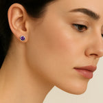 Porträt einer Frau in Seitenansicht, die einen silbernen Ohrstecker mit einem runden, facettierten Amethyst trägt. Der violette Edelstein funkelt dezent im Licht, während die Frau mit glatter Haut und dezentem Make-up vor einem neutralen Hintergrund zu sehen ist.