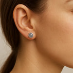 Nahaufnahme einer Frau in Seitenansicht, die einen kleinen silbernen Ohrstecker mit rundem, grauem Cabochon-Stein trägt. Der leicht gewölbte Stein sitzt mittig am Ohrläppchen und schimmert dezent im natürlichen Licht.