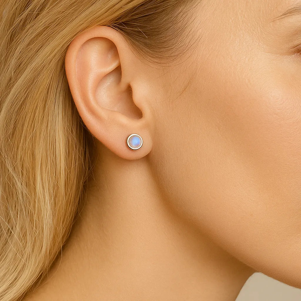 Nahaufnahme einer Frau im Profil mit einem 5 mm großen runden Ohrstecker aus Silber und schimmerndem Mondstein im Ohr. Der Stein zeigt einen dezenten bläulichen Schimmer, der das Licht reflektiert. Die Haut ist glatt, das Haar blond und dezent hinter das Ohr gelegt, um den Ohrring klar hervorzuheben.