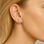 Nahaufnahme einer Frau im Profil mit einem 5 mm großen runden Ohrstecker aus Silber und schimmerndem Mondstein im Ohr. Der Stein zeigt einen dezenten bläulichen Schimmer, der das Licht reflektiert. Die Haut ist glatt, das Haar blond und dezent hinter das Ohr gelegt, um den Ohrring klar hervorzuheben.