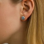 Nahaufnahme einer Frau im Profil mit einem kleinen runden Ohrstecker aus Silber und einem facettierten mystischen Topas im Ohr. Der Stein zeigt schillernde Farbreflexe in Lila-, Blau- und Grüntönen, die im Licht glitzern. Das blonde Haar ist hinter das Ohr gelegt, um den funkelnden Ohrring deutlich hervorzuheben.